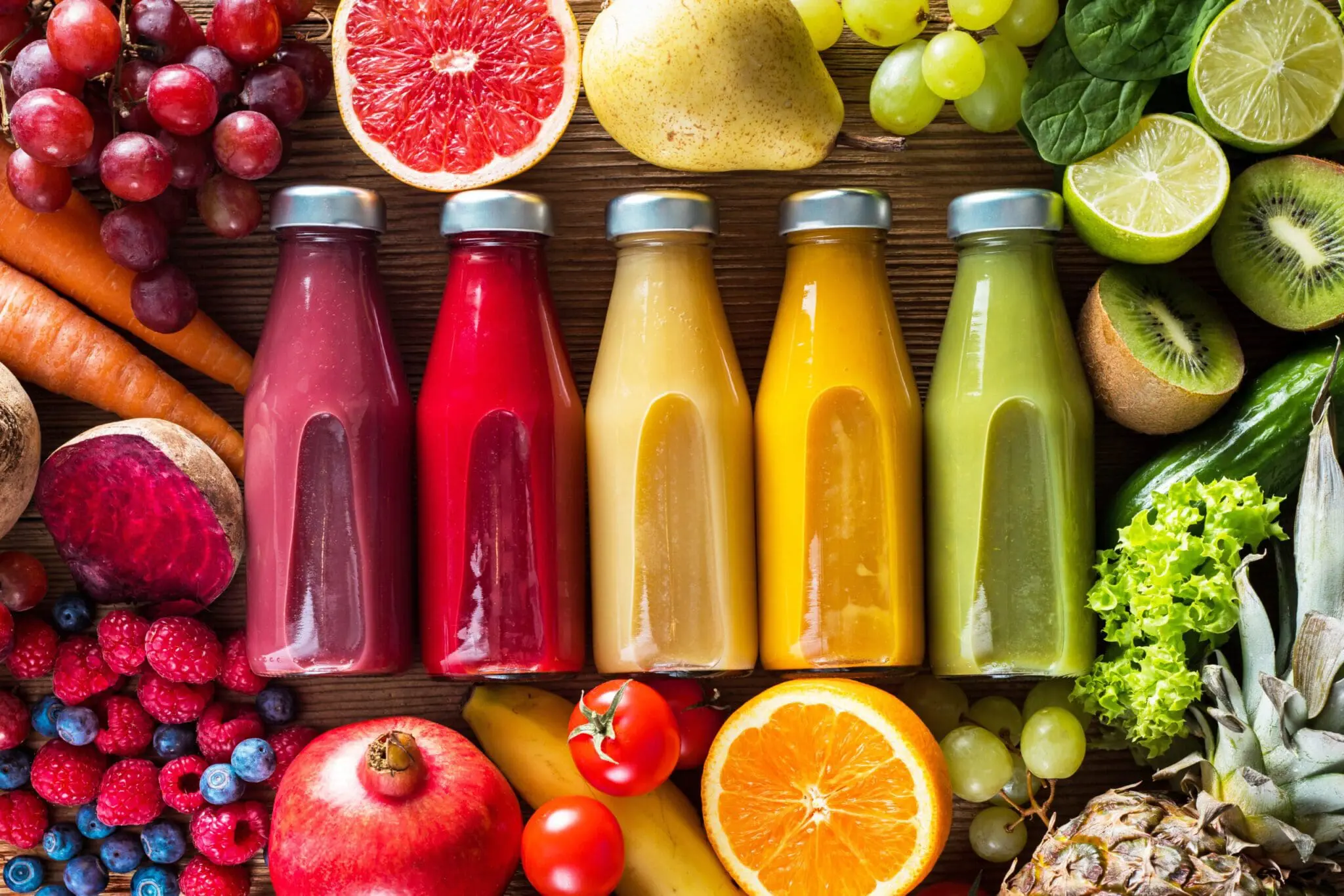 A colorful assortment of juices surrounded by fruits, related to the Nutrition blog post, 'Three Things You Should Never Juice'