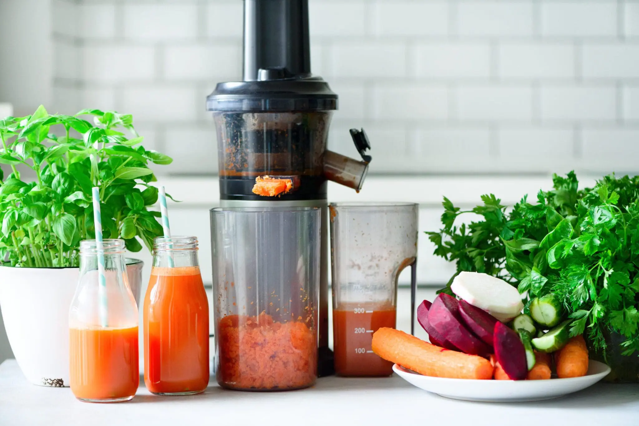 Fresh carrot juice in bottles with a juicer and root vegetables – healthy homemade juice preparation