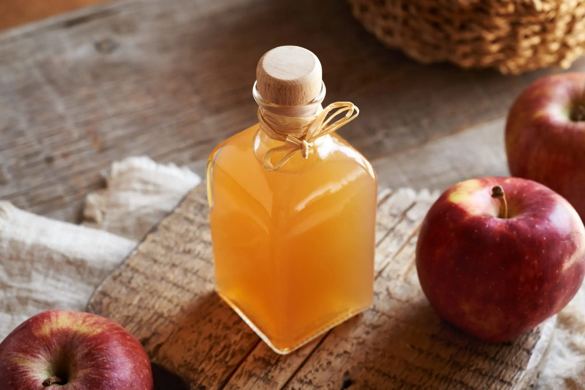 A glass jar of apple cider vinegar on a table surrounded by apples, featured in the blog post 'Health Benefits of Apple Cinder Vinegar'