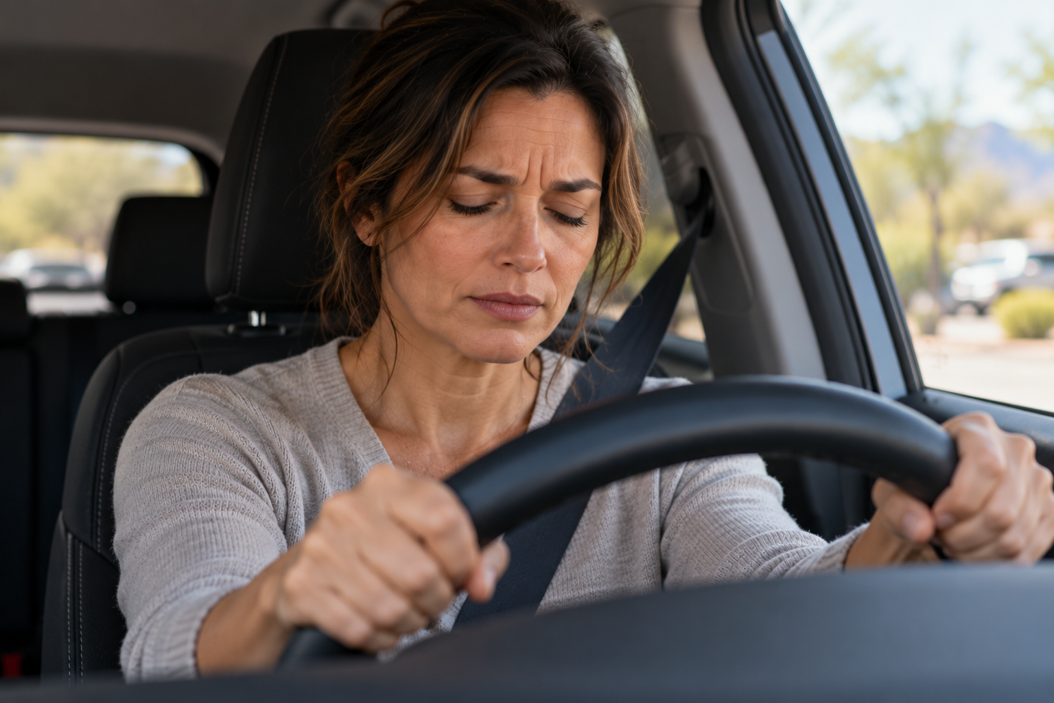 Person in a parked car gripping the steering wheel with eyes closed and a tight jaw, trying to stay composed.