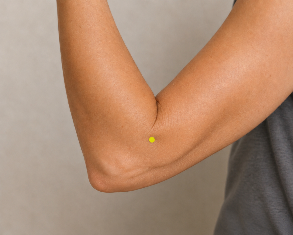 Close-up of a thumb pressing LI11, the acupressure point at the outer end of the elbow crease when the elbow is bent.