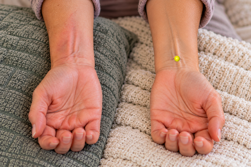 Close-up of two wrists side by side, one resting untouched and the other with a yellow dot marker at the matching spot being gently pressed, indicating a mirror point on the opposite limb.