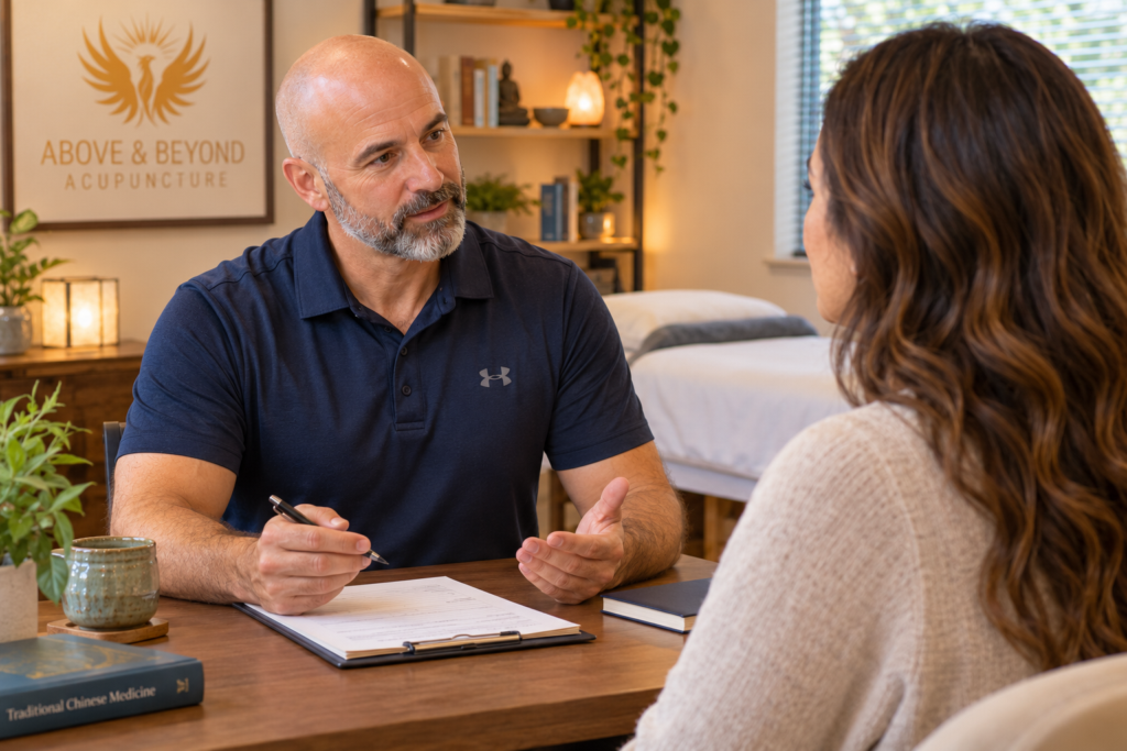 Male acupuncturist speaking with a female patient during an initial consultation in a warm, welcoming acupuncture clinic.