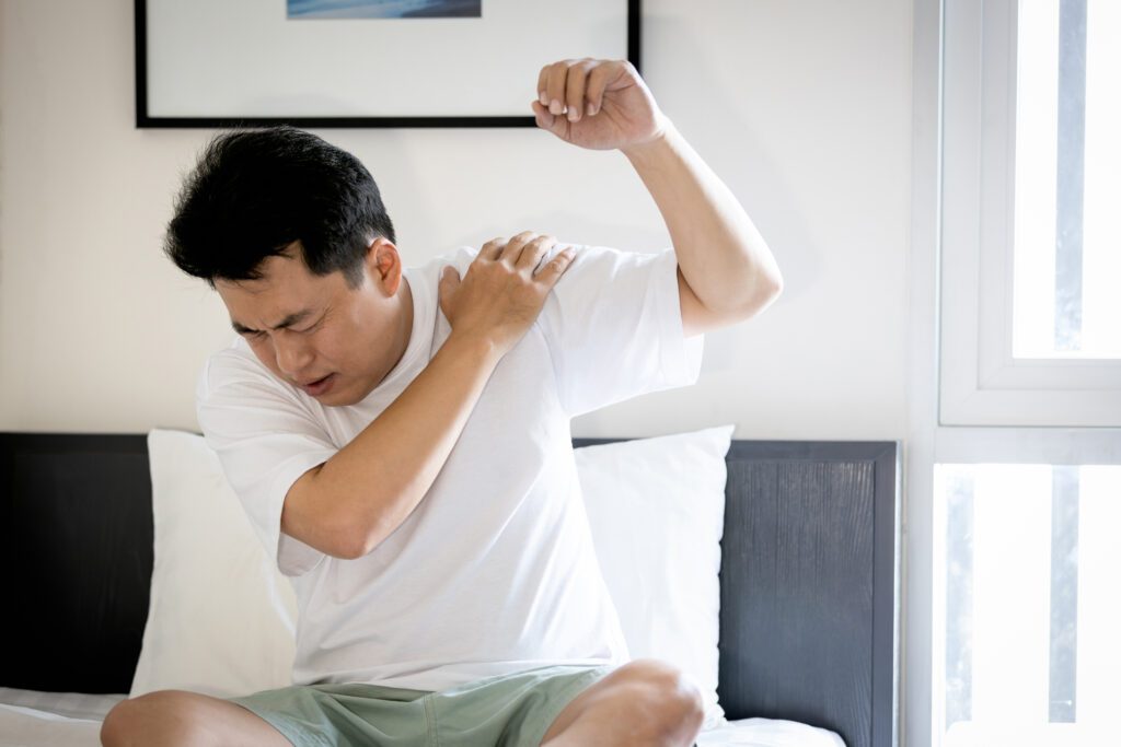 Man holding his shoulder in pain, with one arm raised, expressing discomfort. Related to the Treatment blog post, 'Can Acupuncture Treat Frozen Shoulder?'