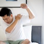 Man holding his shoulder in pain, with one arm raised, expressing discomfort. Related to the Treatment blog post, 'Can Acupuncture Treat Frozen Shoulder?'