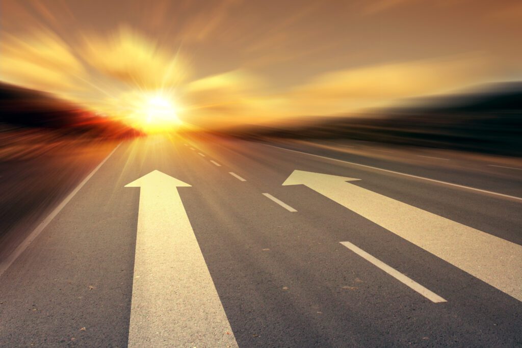 A road stretching into the distance with two arrows pointing forward, leading toward a sunset, symbolizing direction, choice, and the journey ahead. Related to the Lifestyle blog post, 'Keep Moving Forward!'
