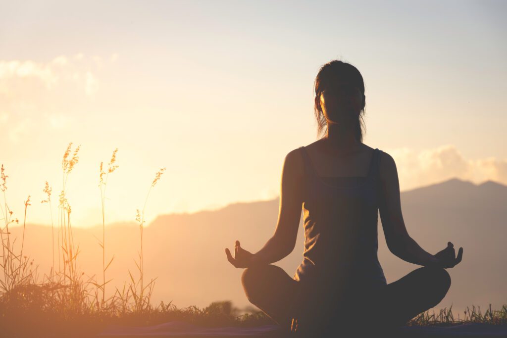 Silhouette of a woman practicing meditation on a mountain during sunrise. Related to the Lifestyle blog post, 'The Many Benefits of Meditation'.