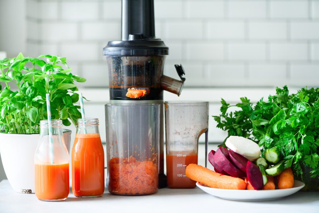 Fresh carrot juice in bottles with a juicer and root vegetables – healthy homemade juice preparation