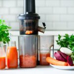 Fresh carrot juice in bottles with a juicer and root vegetables – healthy homemade juice preparation