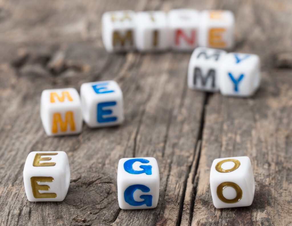 Lettered dice on a wood table spelling out the words: mine, me, my, ego. Featured in the blog post, 'Ego Identification'