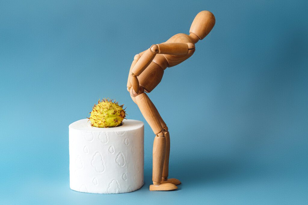 Wooden figure sit on a roll of toilet paper. Concept of the problem with hemorrhoids. Featured in the wellness blog post, 'Having Hemorrhoids? Try Acupuncture!'