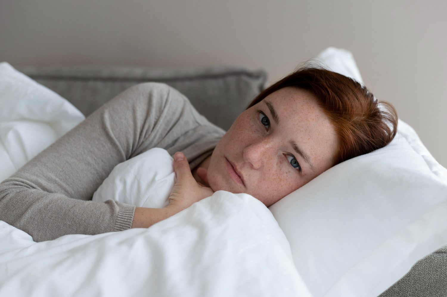 A woman lying awake in bed with a concerned expression, clutching a white pillow.