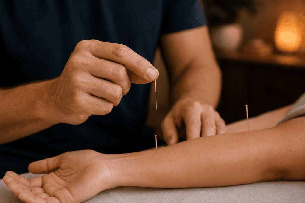 Close-up of an acupuncturist's hands holding a fine acupuncture needle in the precise pinch grip of the technique, just before insertion on a patient's arm.