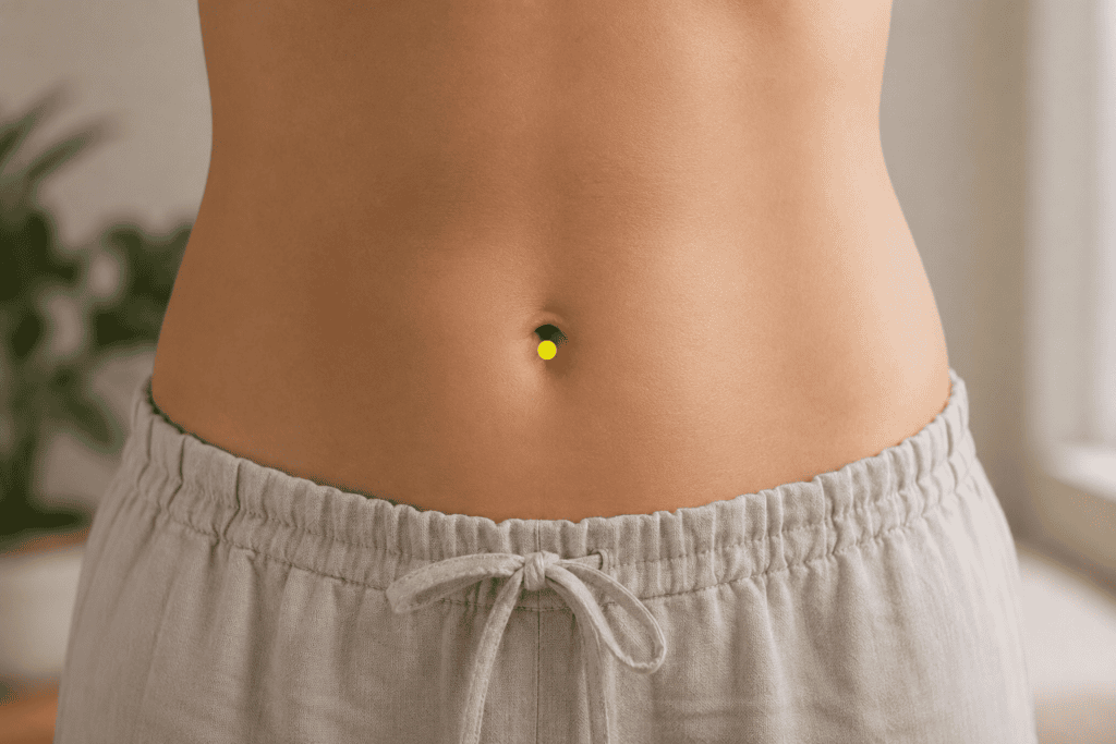 Midsection of a person with a yellow dot marker at the exact center of the navel, indicating the location of CV8.