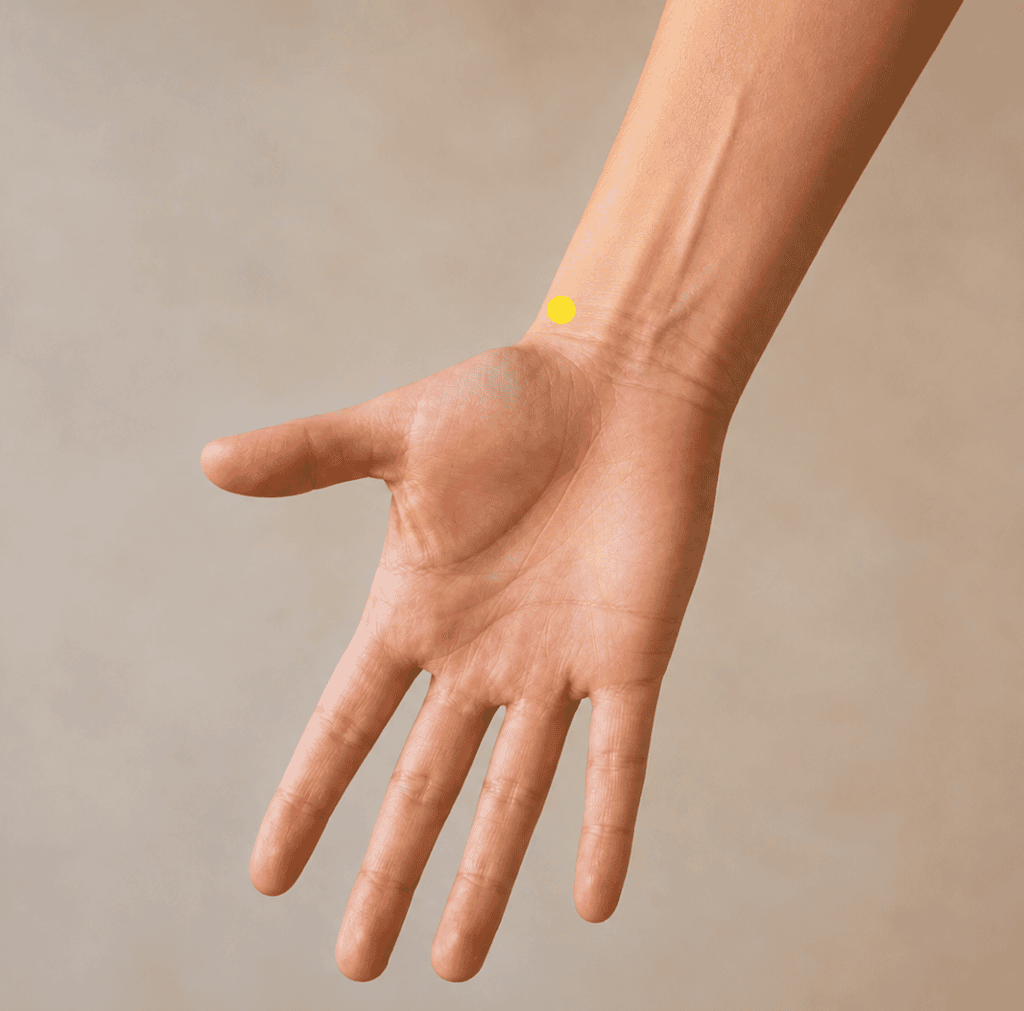 Close-up of a forearm with a yellow dot marker just above the wrist crease on the thumb side, indicating LU7.