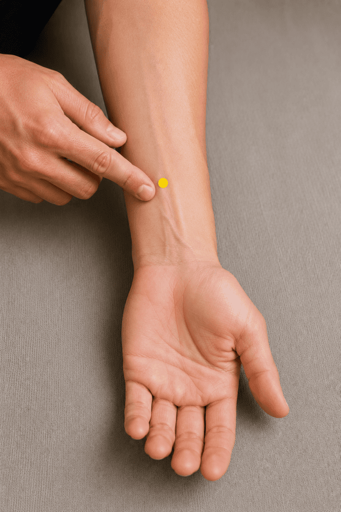 Close-up of an inner forearm with a yellow dot marker about three finger-widths above the wrist crease between the two tendons, indicating the location of PC6.