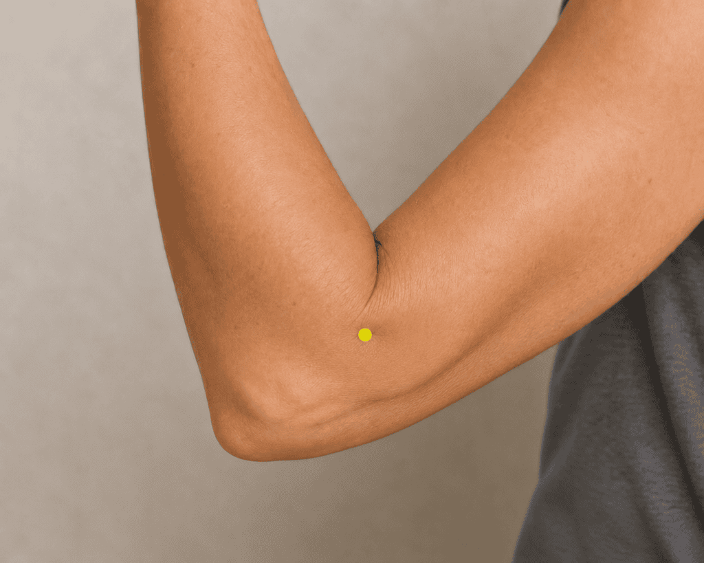 Close-up of a bent elbow with a yellow dot marker at the outer end of the elbow crease, indicating LI11.