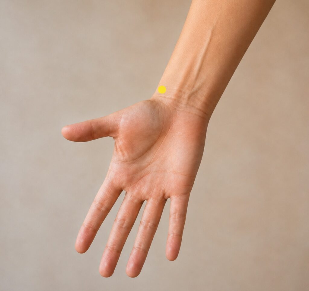 Close-up of a forearm with a yellow dot marker just above the wrist crease on the thumb side, indicating LU7.