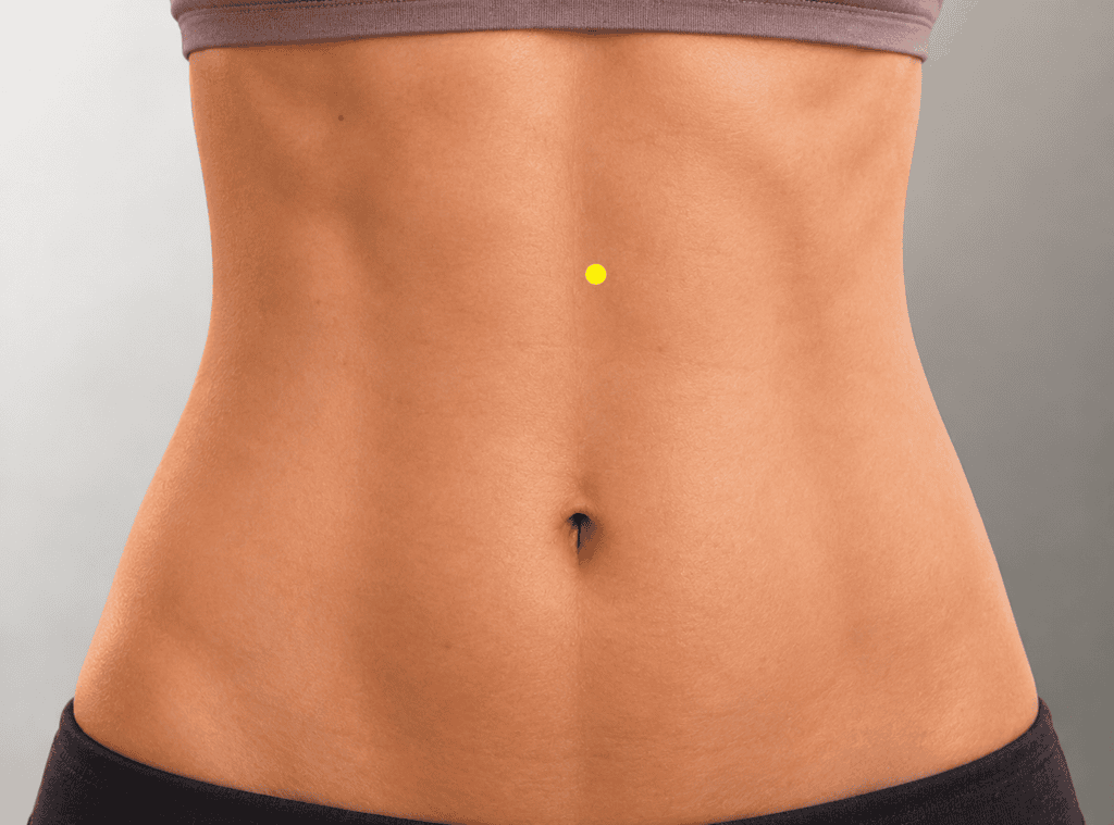 Close-up of a modestly framed upper abdomen with a yellow dot marker about six finger-widths above the navel and half a thumb-width lateral to the midline, indicating the location of KI21.